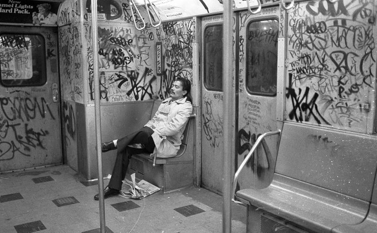 1980's: The writing's on the wall: A tired passenger rests while seated in an empty, graffiti-filled subway car in 1980.