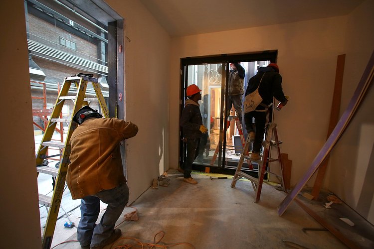 Workers installing a sliding window in the main living area of an apartment.