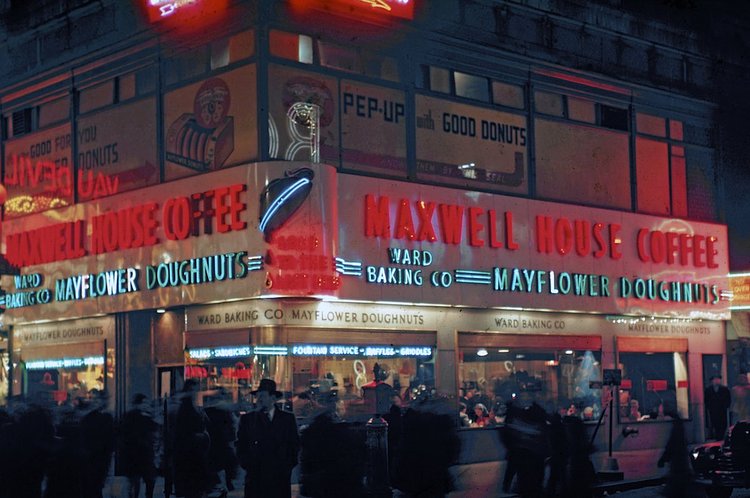 1946 The neon-illuminated Maxwell House and Mayflower Doughnuts coffee shop at the north-west corner of the busy intersection of West 42th Street (which runs left to right) and Broadway.