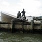 NYC - Battery Park: American Merchant Mariners Memorial | Commissioned by the American Merchant Mariners' Memorial, Inc., this memorial was conceived in 1976. In 1988, after an extensive competition, the artist Marisol Escobar (b. 1930), known as Marisol, was chosen to develop her design. Situated off-shore from the north end of Battery Park and just south of Pier A, the monument stands on a rebuilt stone breakwater in the harbor. The bronze figural group and boat are based on an actual historical event; during World War II, a Nazi U-boat attacked a merchant marine vessel, and while the marines clung to their sinking vessel, the Germans photographed their victims. Marisol developed a series of studio sketches from this photograph, then fashioned a clay maquette as her winning design proposal for the monument. The work was dedicated on October 8, 1991.