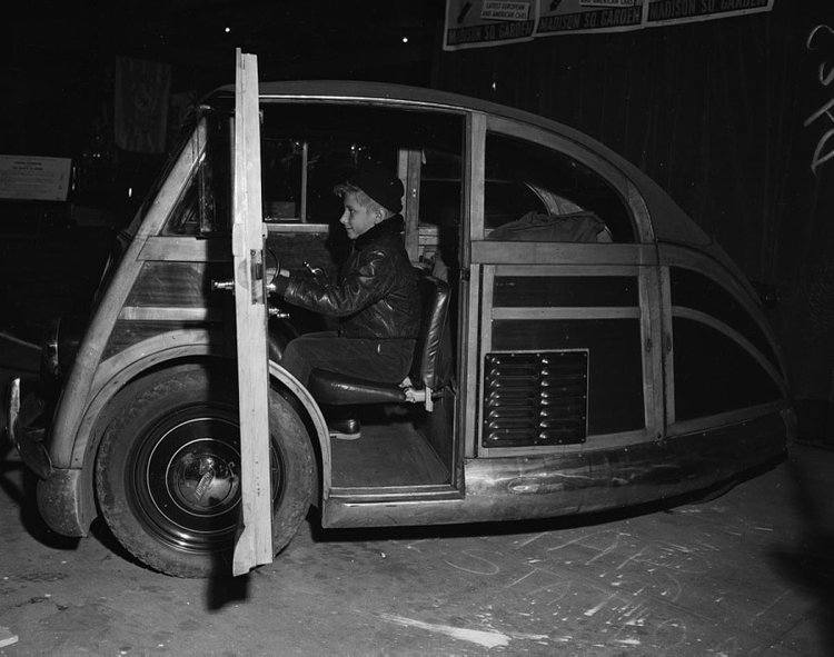 Give this little fellow credit for having such a determined look while behind the wheel of…well, we’re not entirely sure! Can anyone guess the name of this bizarre wood-bodied vehicle?