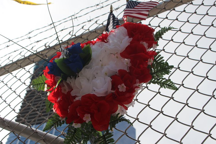 detail shot | An American flag and order of flowers hung on a fence outside of the World Trade Center Site. Photo by Brelaun Douglas.