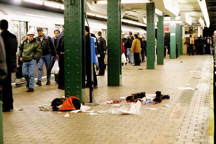 1990's: Subway riders walk by a horrific crime scene on the platform of the 125 St. station after an unidentified person was shot, leaving behind a pool of blood and clothing of the victim.