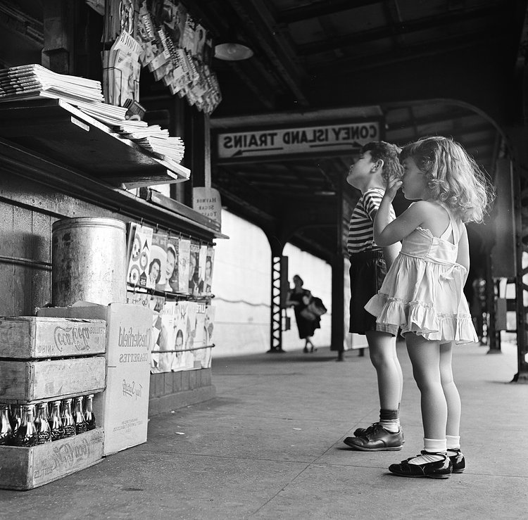 A brother and his sister look up at a newsstand, located on the platform of the New York city subway, as they wait for the train to Coney Island, New York, 1948.