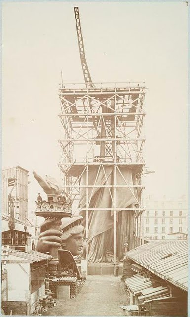 Assemblage of the Statue of Liberty in Paris, showing the bottom half of the statue erect under scaffolding, the head and torch at its feet, 1883.