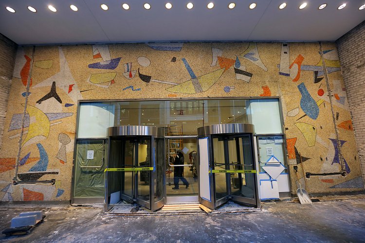 A mural by Max Spivak at the base of the 5 Bryant Park office tower in Manhattan includes shapes that appear abstract at first, but closer inspection reveals them to be textile makers’ tools, like a T-square, above the entrance.
