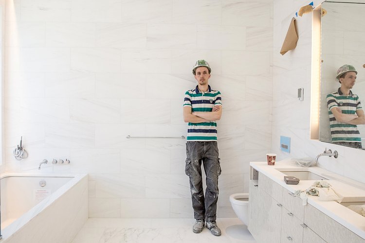 Here the artist leans against the wall of a master bathroom. Behind the tiles, lies a self-portrait, he helped tile over himself.