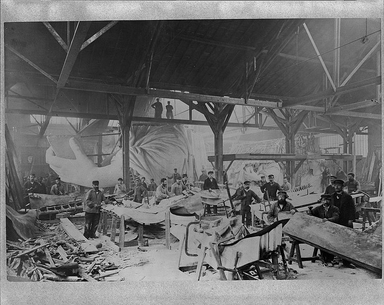 Workmen constructing the Statue of Liberty in Bartholdi's Parisian warehouse workshop; first model; left hand; and quarter-size head-, ca. 1882.