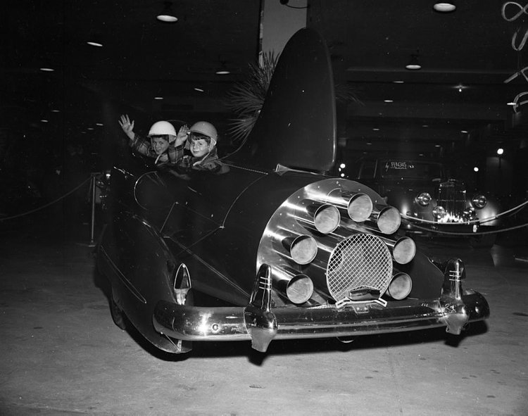 At least they have helmets on! These two tikes are ready for take-off in the “Comet car,” at the Motor Sports Show at Madison Square Garden.
