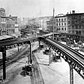 This is an 1878 view of the Third Avenue Line El train tracks, looking north up the east side of the Bowery, at Chatham Square in lower Manhattan, New York.