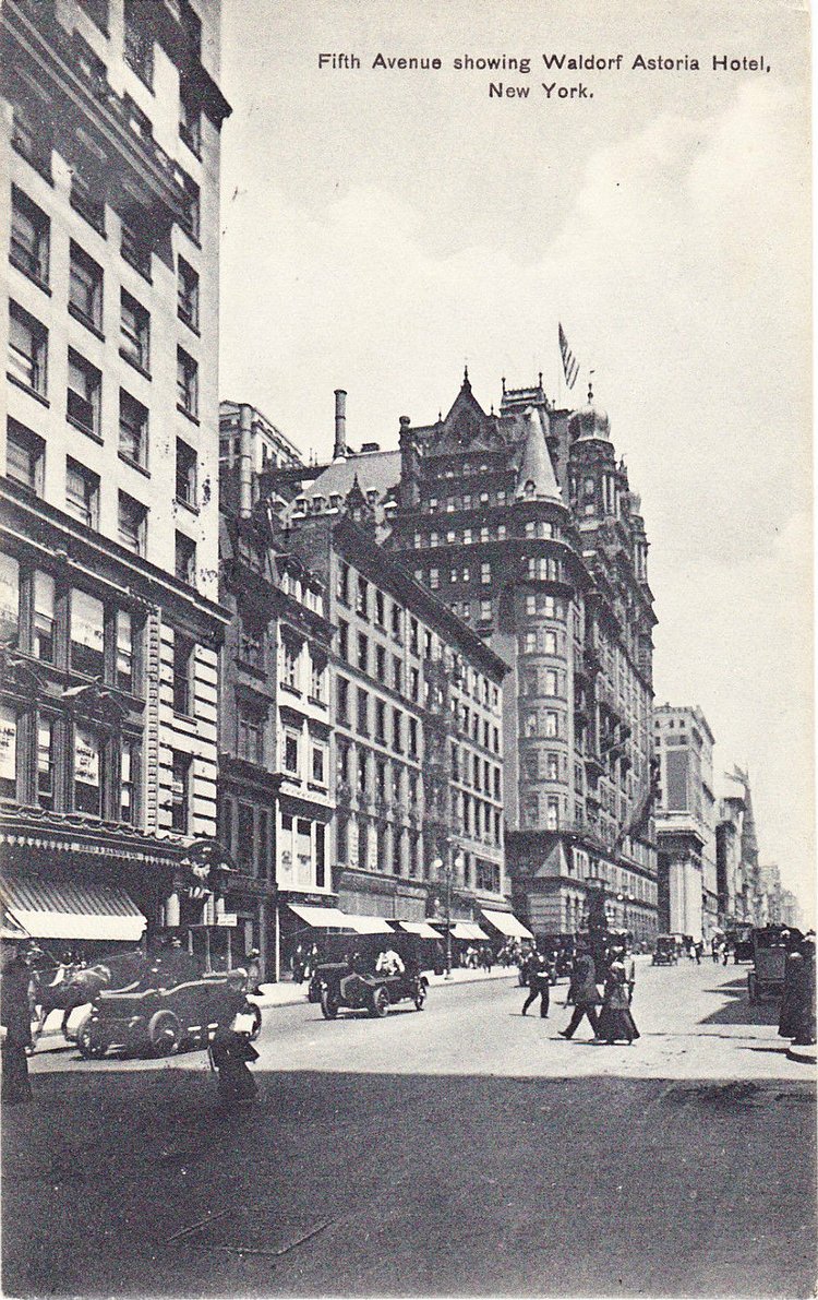 This photo postcard taken around 1915 is looking north on Fifth Avenue from 32nd Street. The turreted Waldorf-Astoria Hotel with its American flag raised on the roof is the focal point of this scene. There are no traffic signals to interrupt the  vehicular traffic on the avenue. People cross the street with little difficulty as the traffic is light.