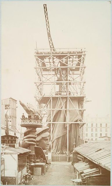 Assemblage of the Statue of Liberty in Paris, showing the bottom half of the statue erect under scaffolding, the head and torch at its feet, 1883.