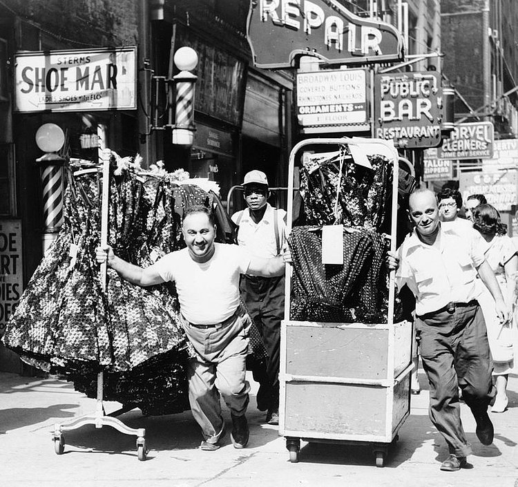 Men pulling racks of clothing on busy sidewalk in Garment District, New York City