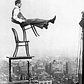 A daredevil balances on the back legs of a chair atop other furniture, 20 stories up in New York, circa 1920. 